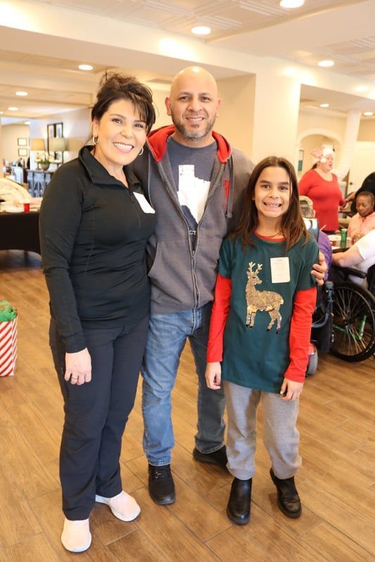 Three people stand smiling together in a brightly lit indoor space, dressed in casual clothing.