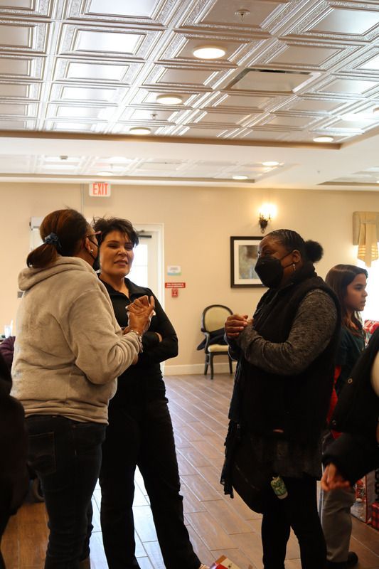 Three people stand in a brightly lit room with a decorative ceiling, engaged in conversation.