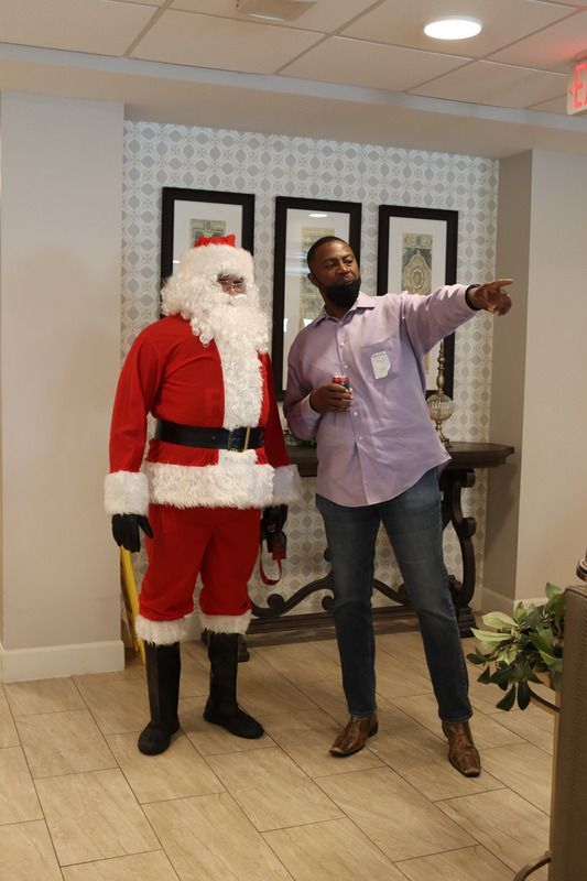 A person in a Santa Claus costume stands next to another individual in a light purple shirt who is pointing away.