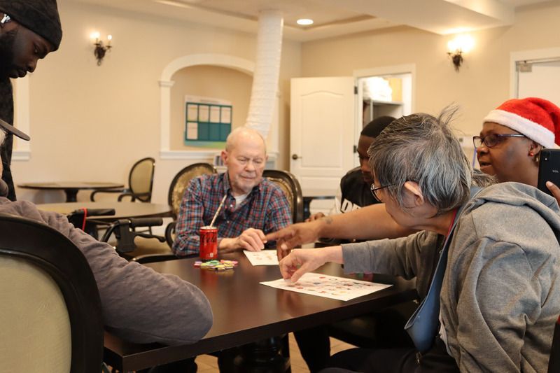 A group of people sit around a table in a brightly lit room, playing a card or board game together.