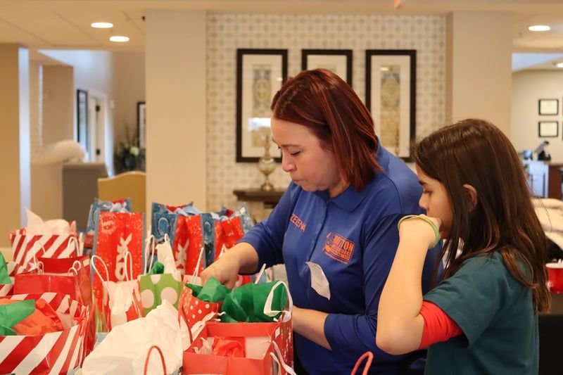 An adult and child packing colorful gift bags in a bright indoor community space.