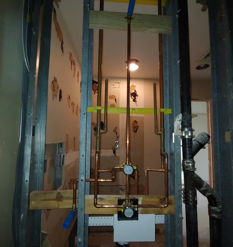 Plumbing installation featuring copper pipes connected to a shower valve inside a wall cavity with metal studs.