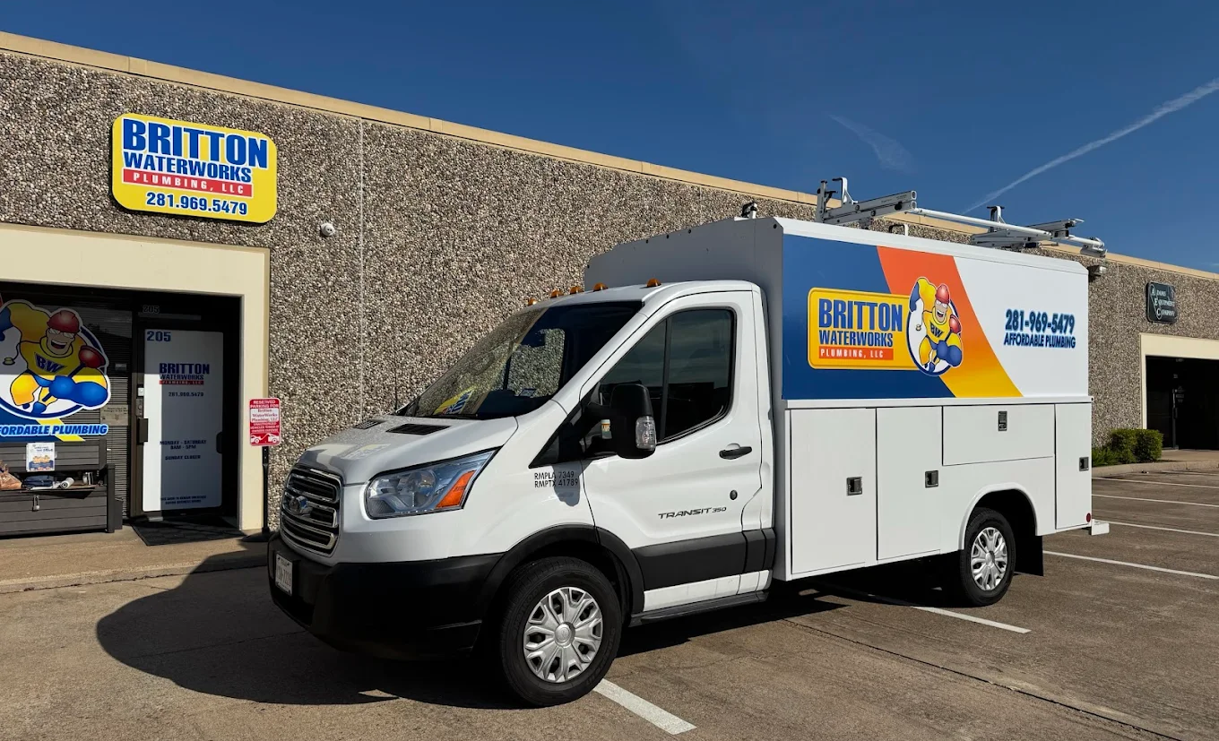 A white Britton Plumbing service van parked outside their office building on a sunny day.