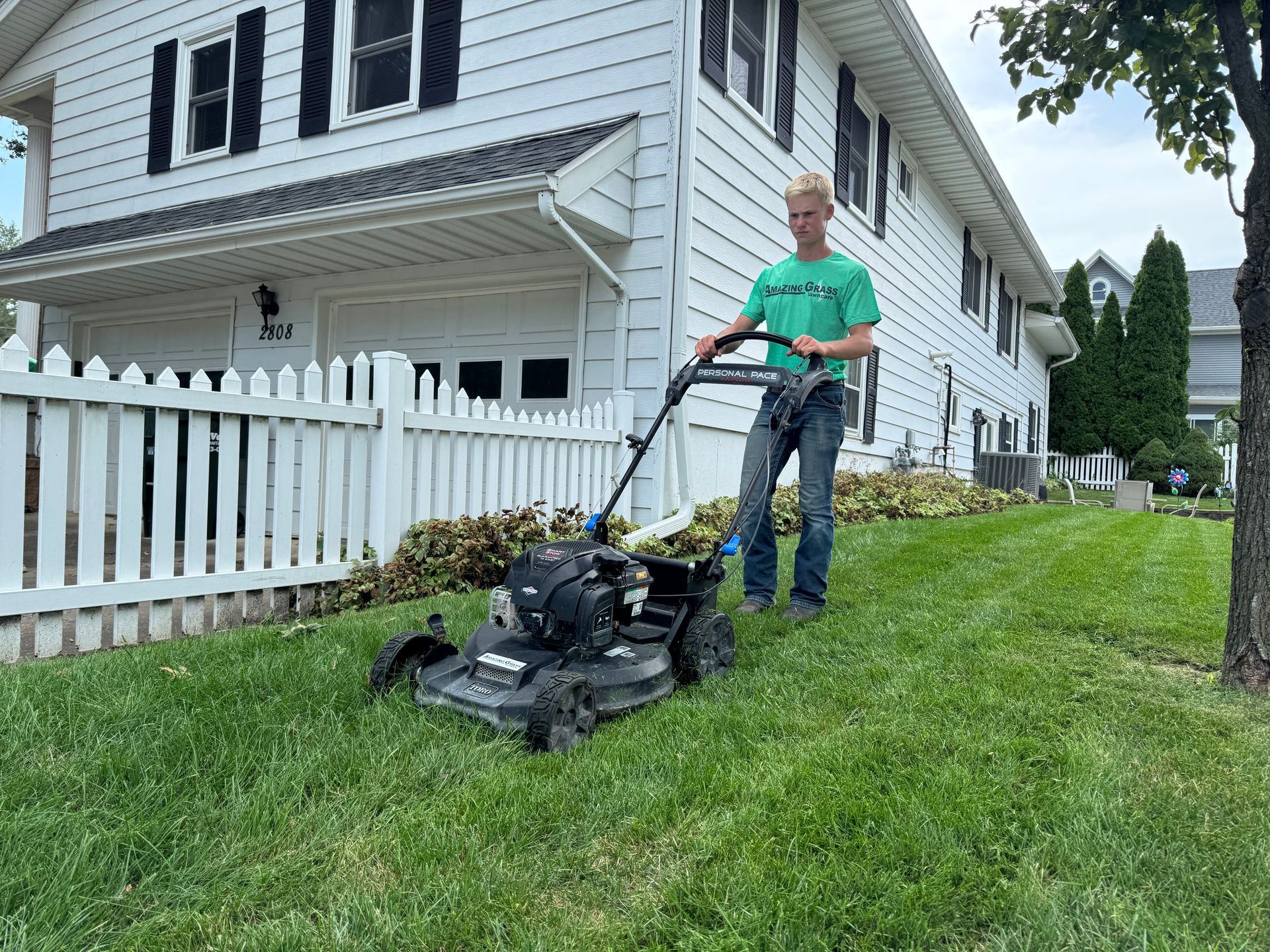 Man mowing a sloped lawn beside a white house and picket fence