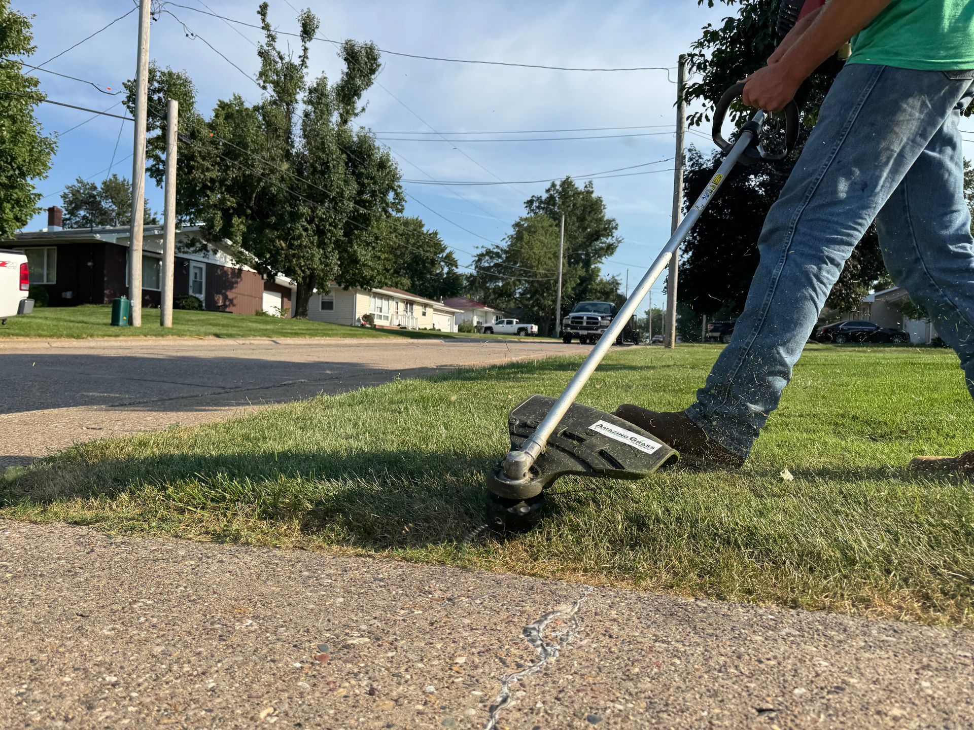 Person using a string trimmer to cut grass along a curb in a suburban yard