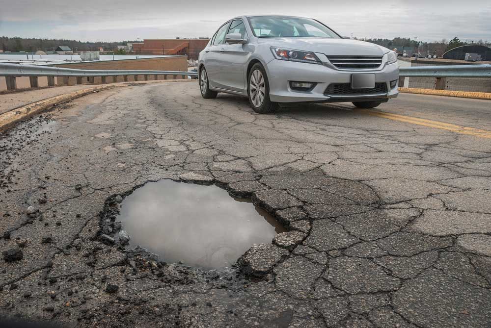 A car is driving through a pothole on a road — Hydro Excavation in Goulburn, NSW