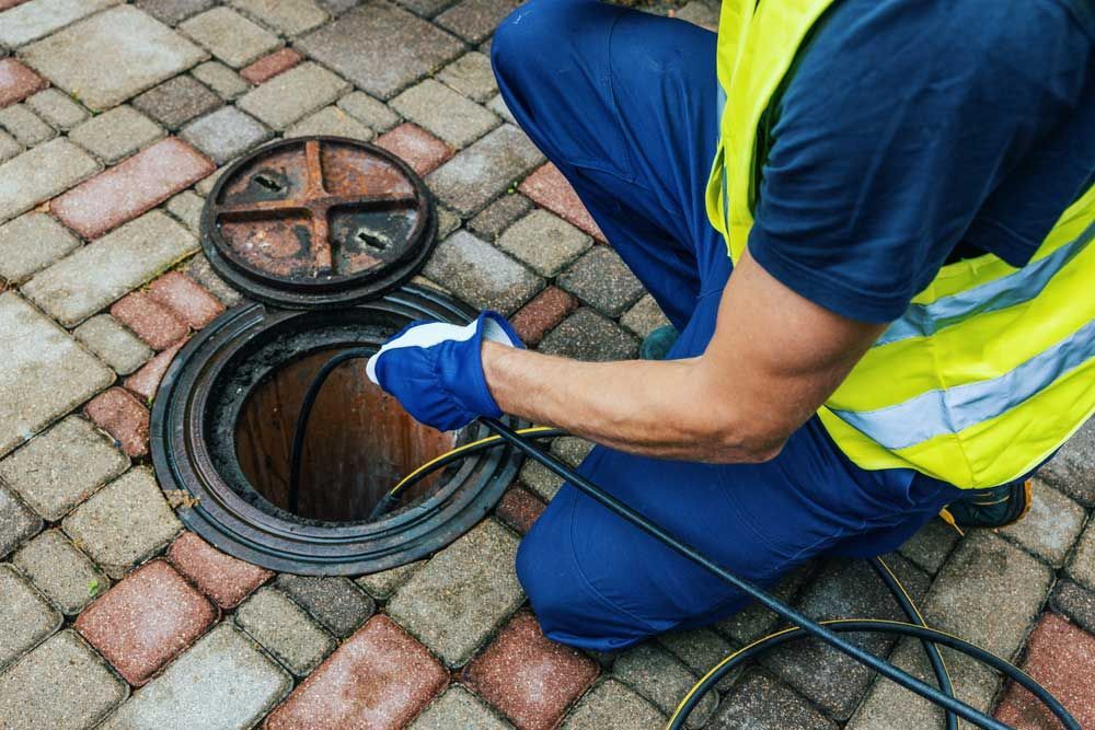 A man is kneeling down in front of a manhole cover — Hydro Excavation in Canberra, NSW