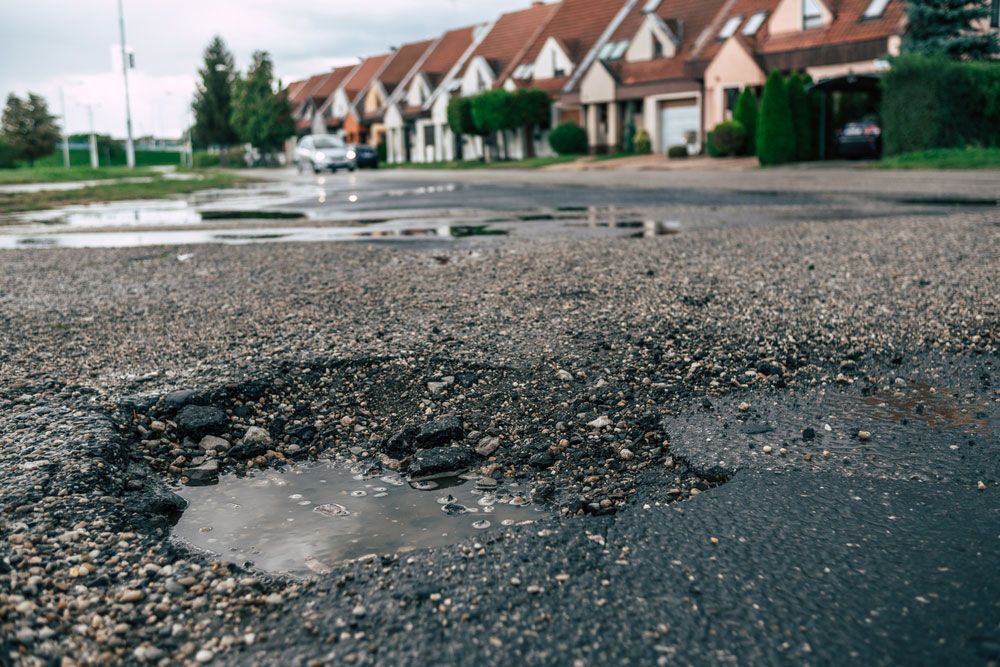 A pothole in the middle of a road in front of a row of houses — Hydro Excavation in Queanbeyan, NSW