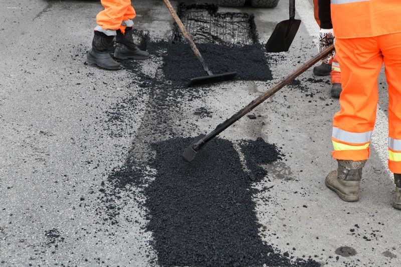 A man is spreading asphalt on the ground with a shovel — Hydro Excavation in Campbelltown, NSW