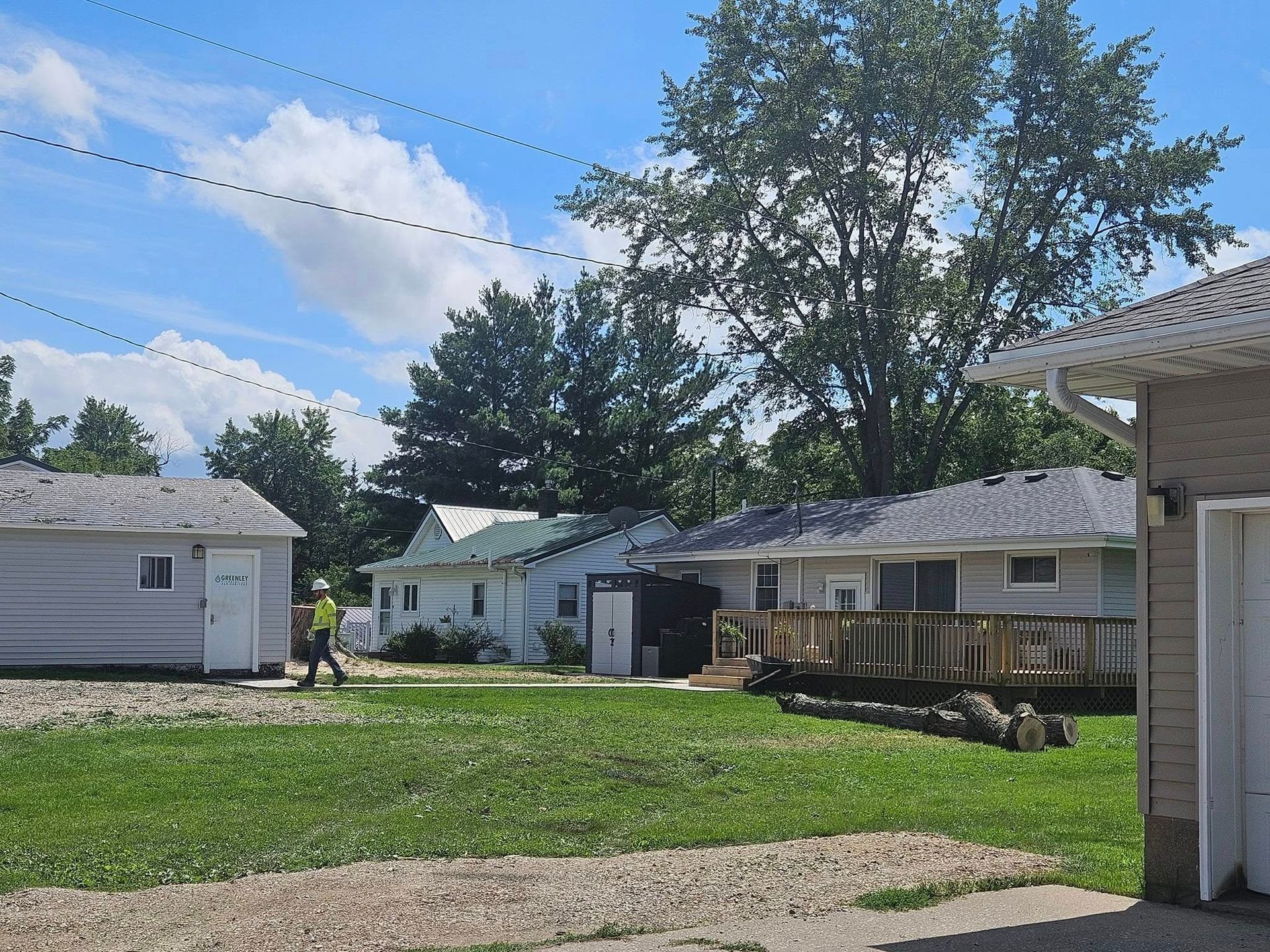 Residential backyard with grass, trees, and single-story houses under a partly cloudy sky