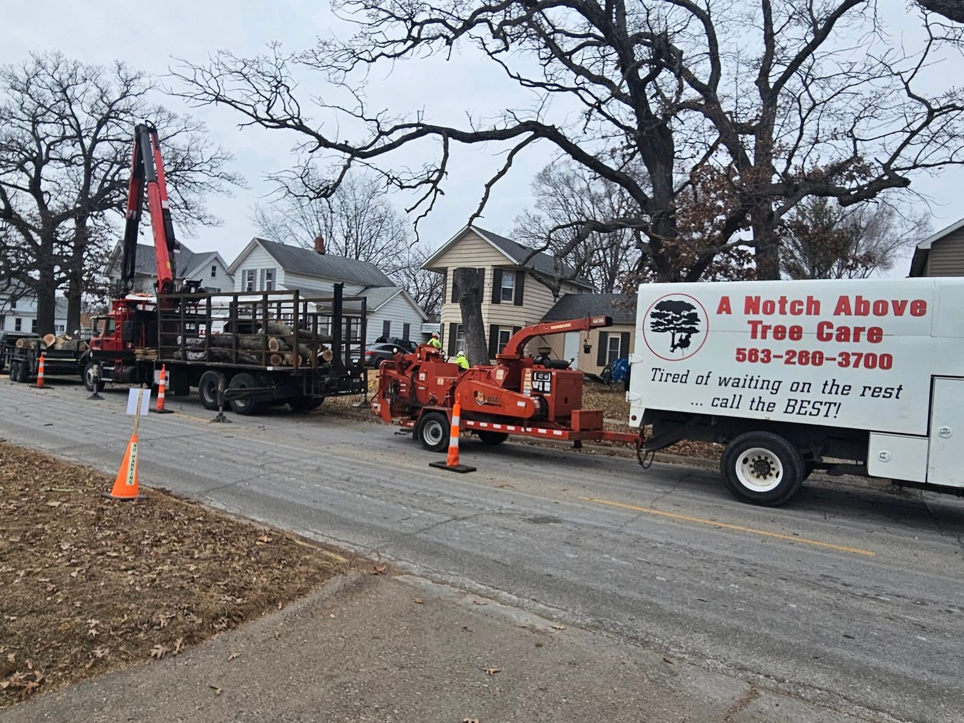Utility truck and cherry picker working on roadside trees near houses in winter