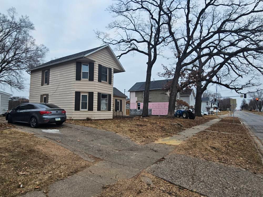 Two-story beige house with a black car parked beside it on a quiet residential street in winter.
