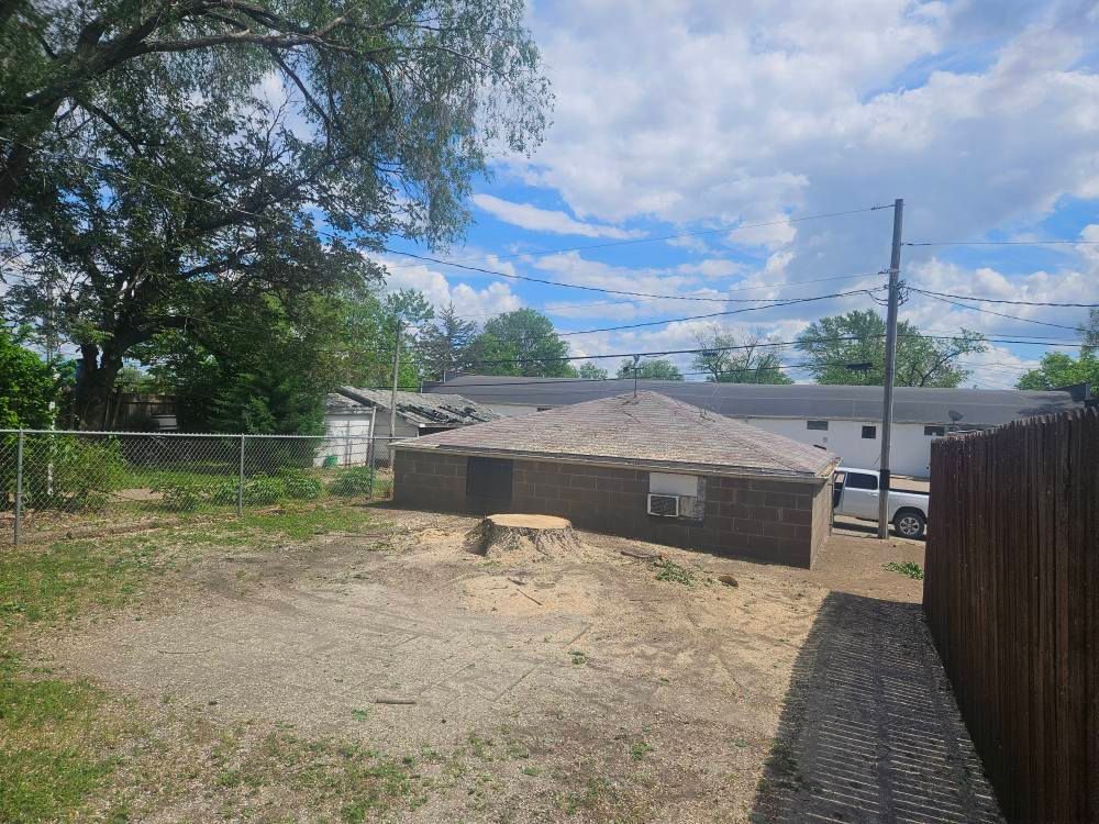 Backyard with bare dirt, a low brick structure, trees, chain-link fence, and a brown wooden fence under a cloudy sky