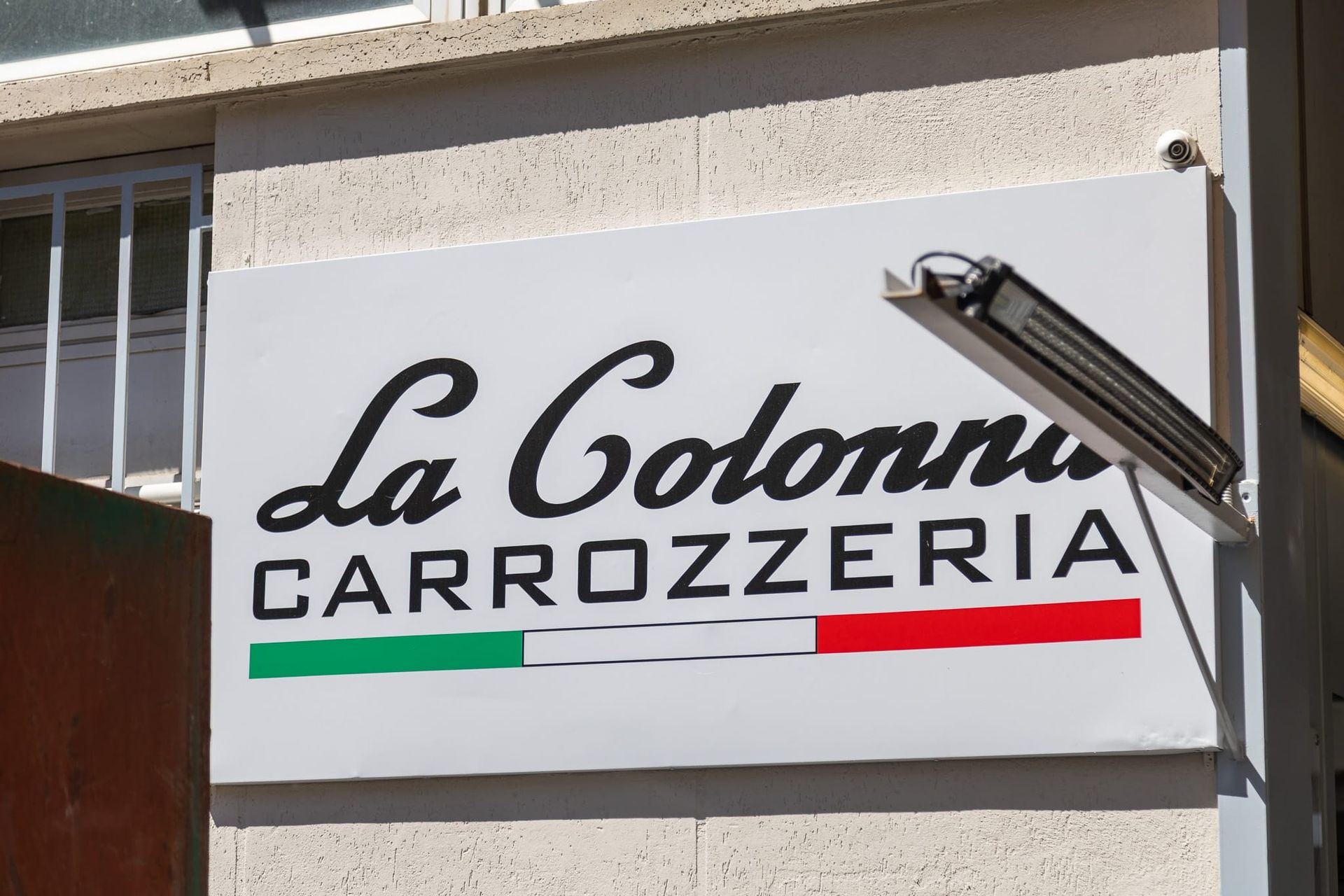 Insegna della Carrozzeria La Colonna su una parete bianca dell'edificio con strisce verdi, bianche e rosse.