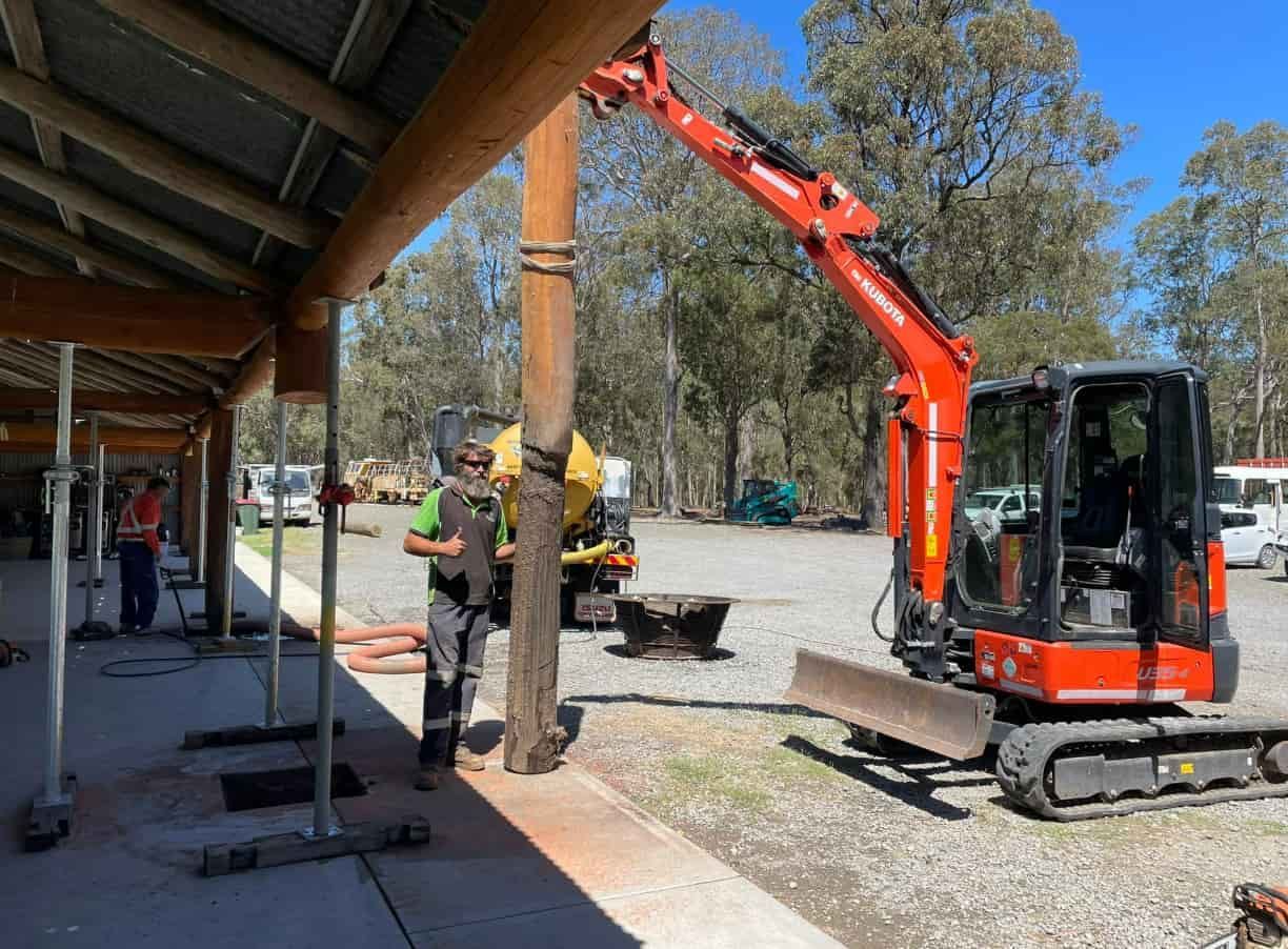 A Man Is Standing Next To A Red Excavator In A Parking Lot — East Coast Locating Services In Maitland, NSW