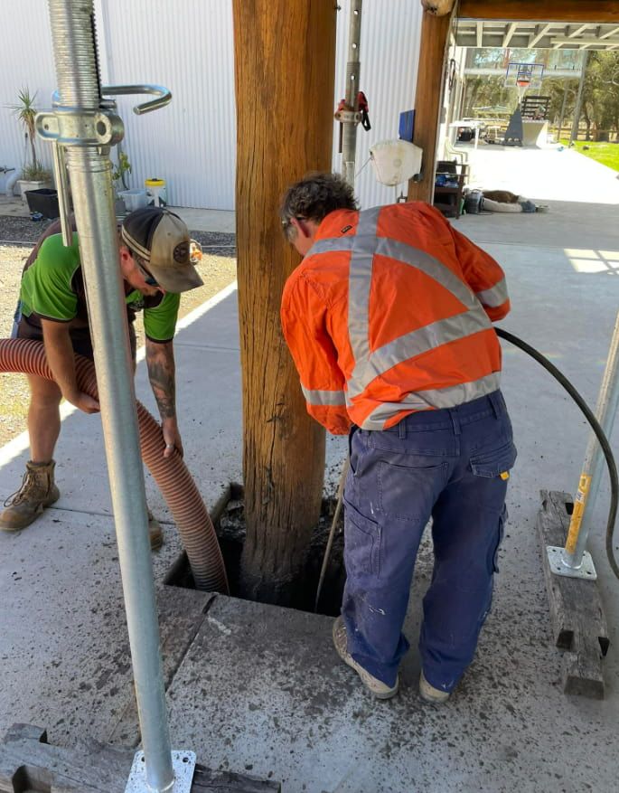 Two Men Are Working On A Wooden Post With A Hose — East Coast Locating Services In Wyong, NSW