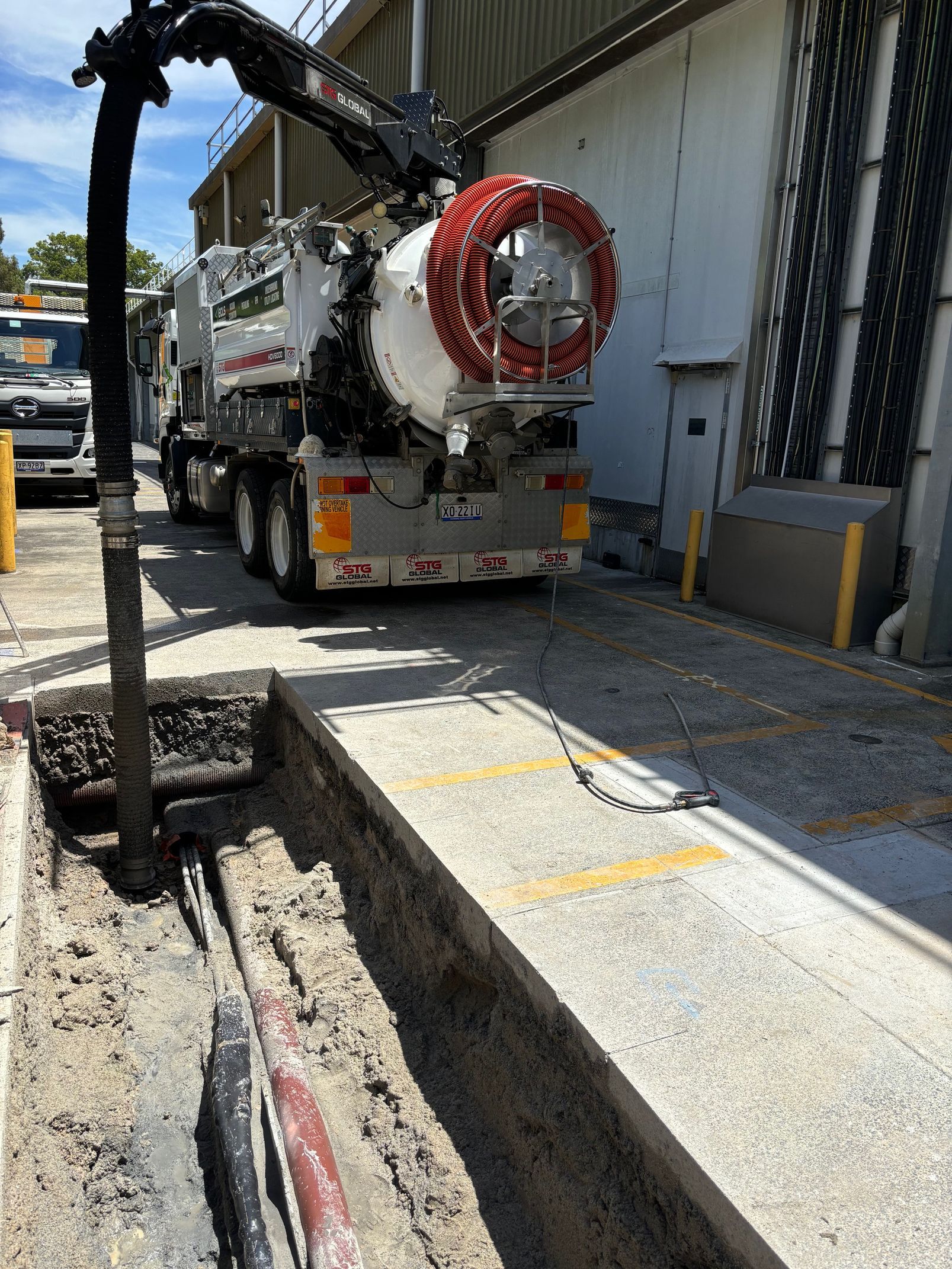A vacuum truck is cleaning a hole in the ground in front of a building.