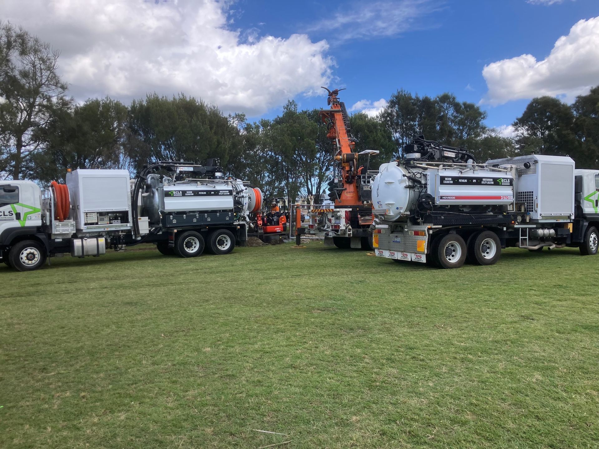 A row of vacuum trucks are parked in a grassy field.
