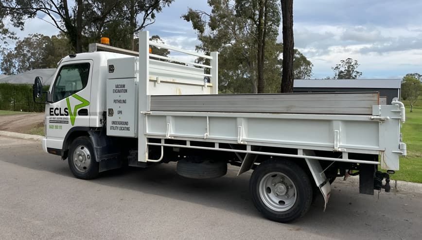 A White Dump Truck Is Parked On The Side Of The Road — East Coast Locating Services In Wallalong, NSW