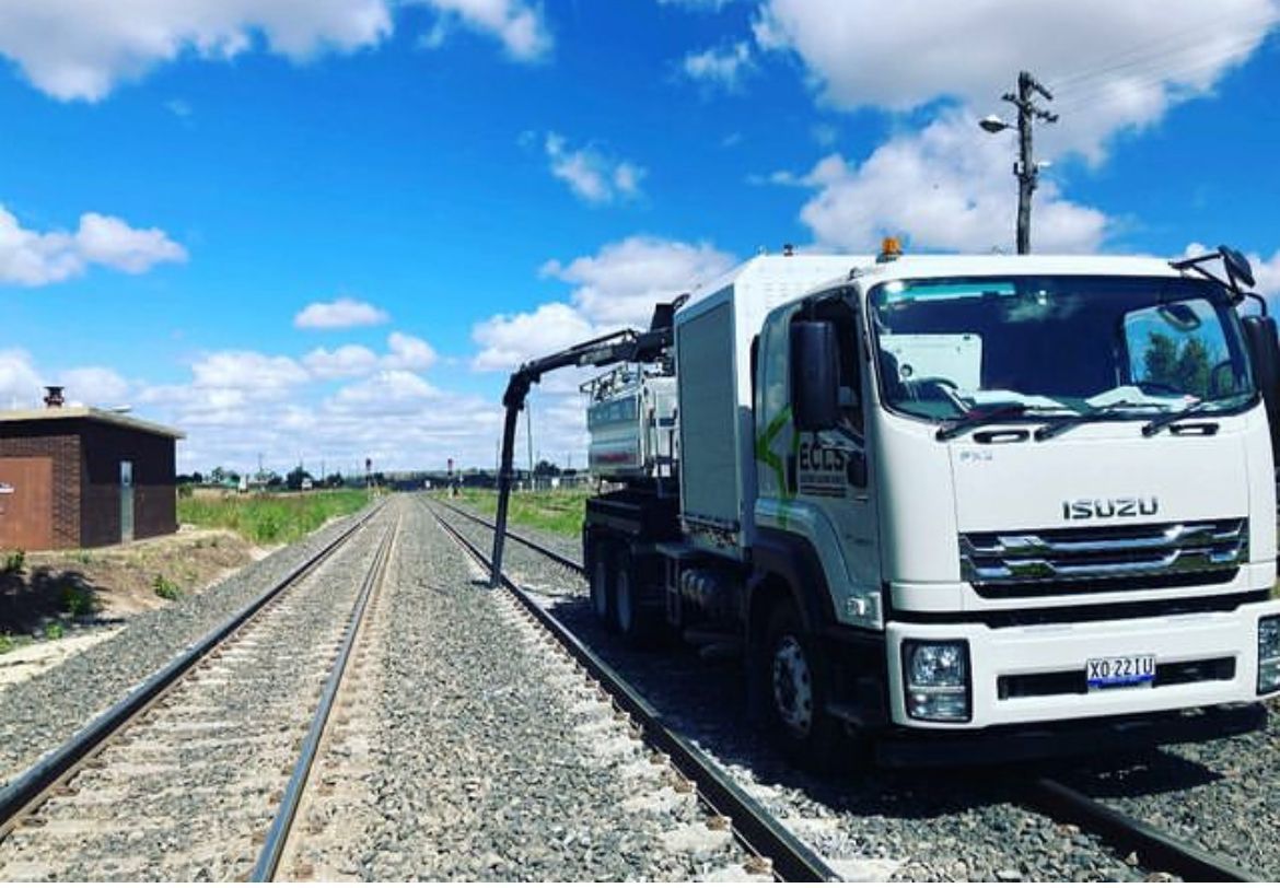 A white truck is parked next to train tracks.