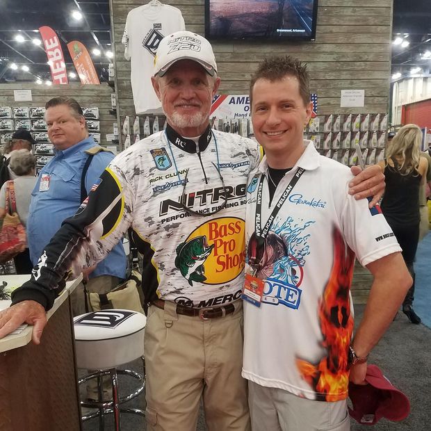 two men are posing for a picture in a store . one of the men is wearing a shirt that says bass pro shop .