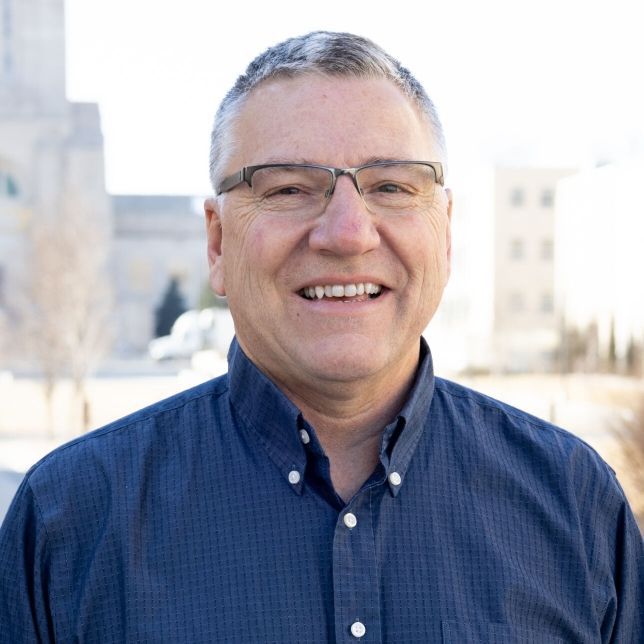 A man wearing glasses and a blue shirt is smiling for the camera.