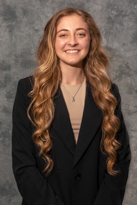 A woman with long hair is wearing a black jacket and a necklace.