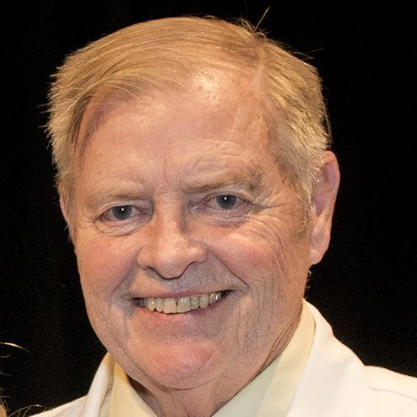 A man wearing a white lab coat and a yellow shirt is smiling.