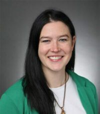 A woman wearing a green jacket and a white shirt is smiling for the camera.