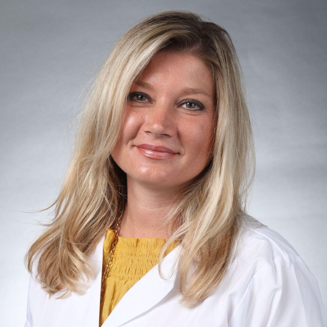 A woman is wearing a white lab coat and a yellow shirt.