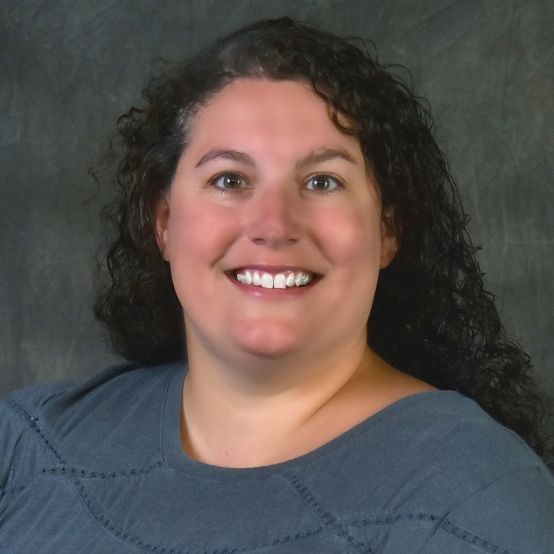 A woman with curly hair is smiling and wearing a blue shirt