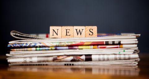A stack of newspapers with the word news written on wooden blocks.