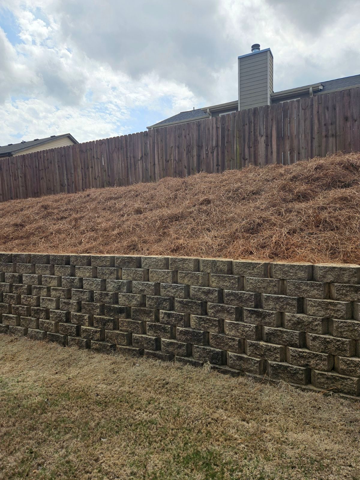 A stone wall is sitting on top of a grassy hill next to a wooden fence.