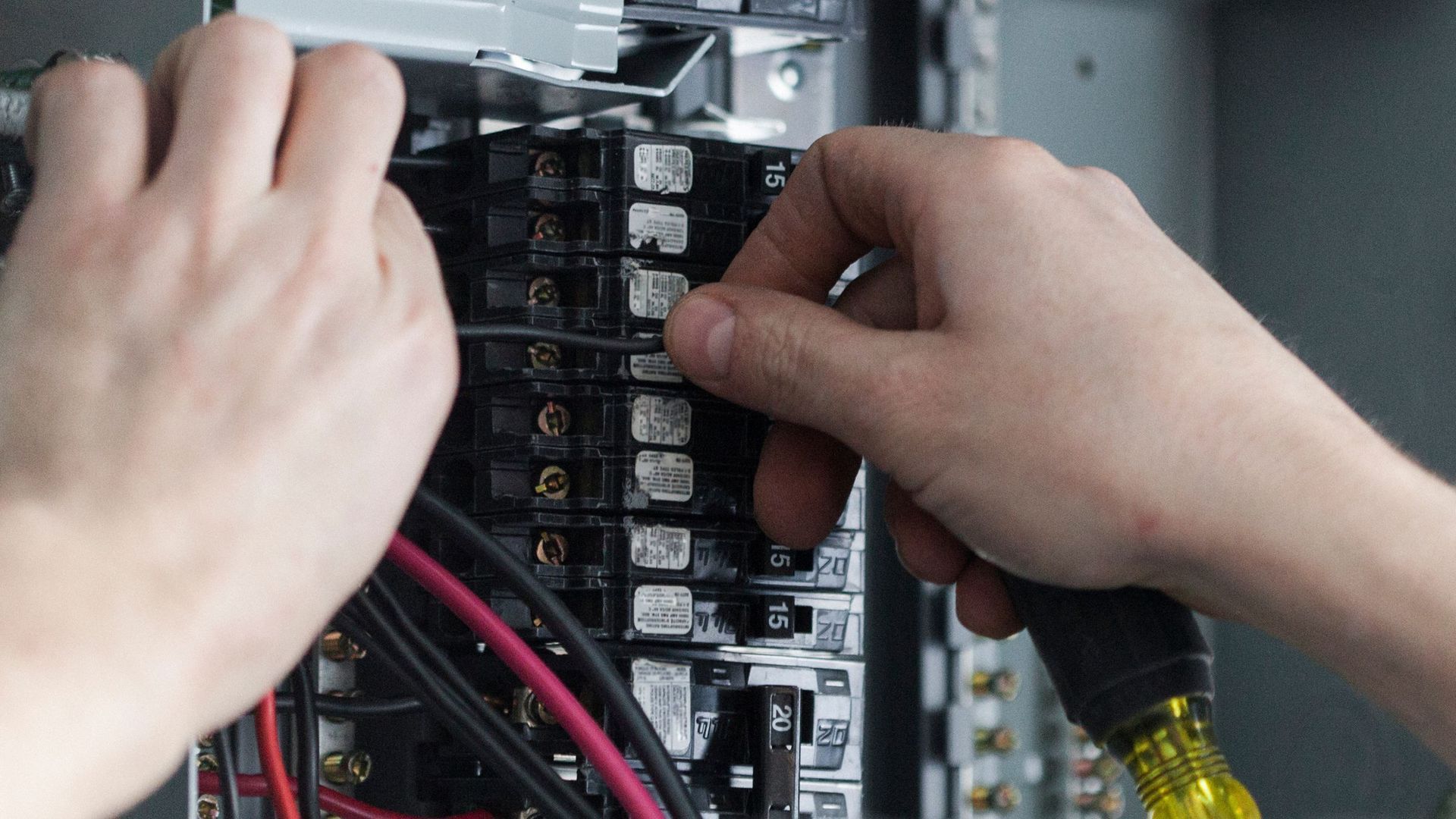 A person is working on an electrical box with a screwdriver.