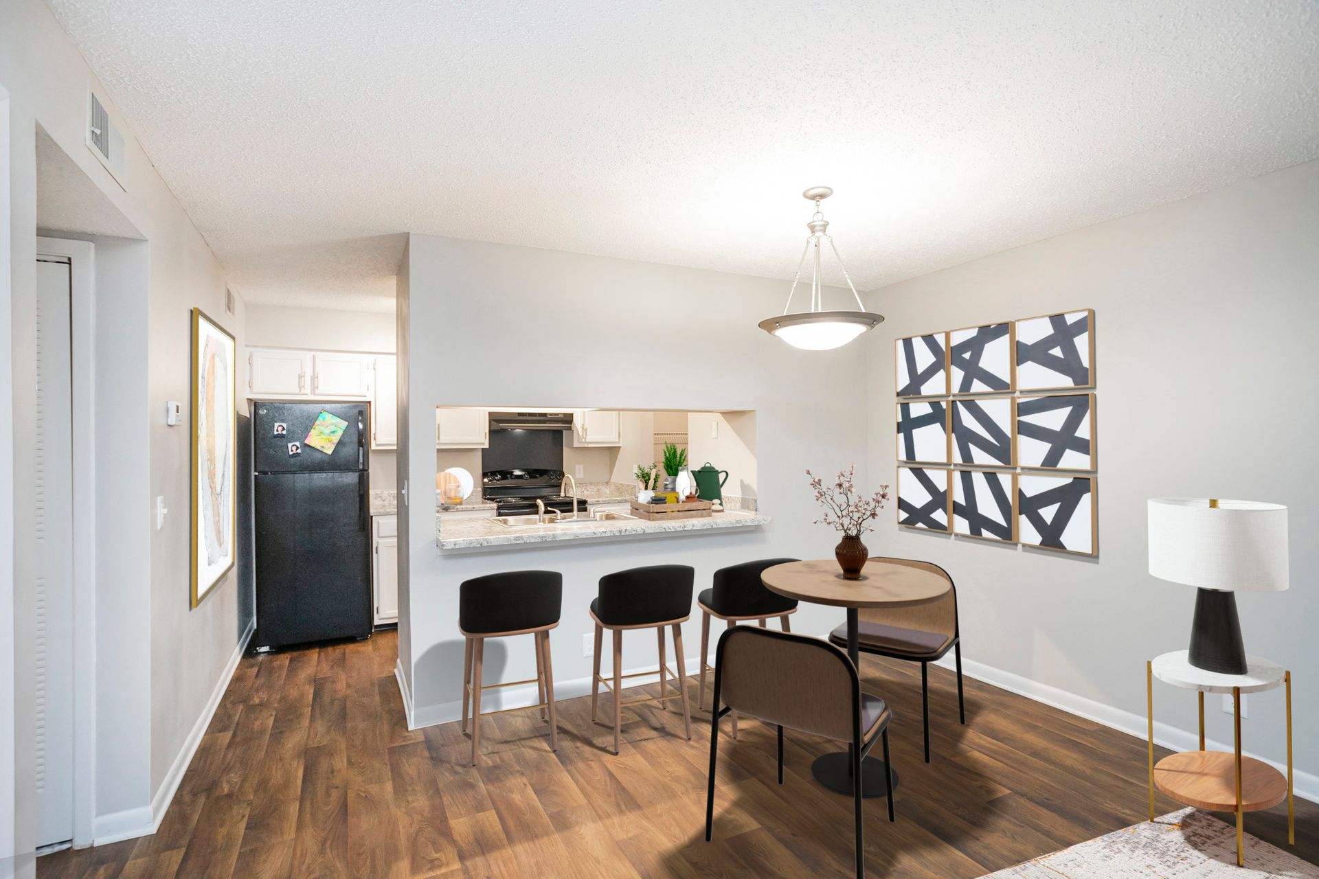 Dining area with a breakfast bar, stools, round table, and hanging light fixture, adjacent to a kitchen with a fridge.