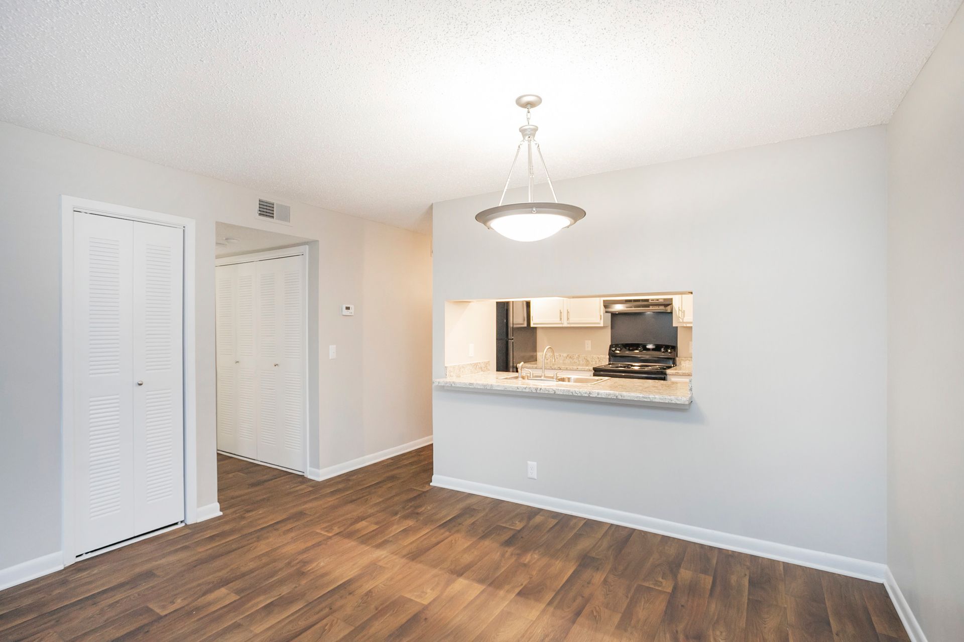 A dining area with wood-look flooring, a hanging light fixture, and a pass-through opening looking into a kitchen.