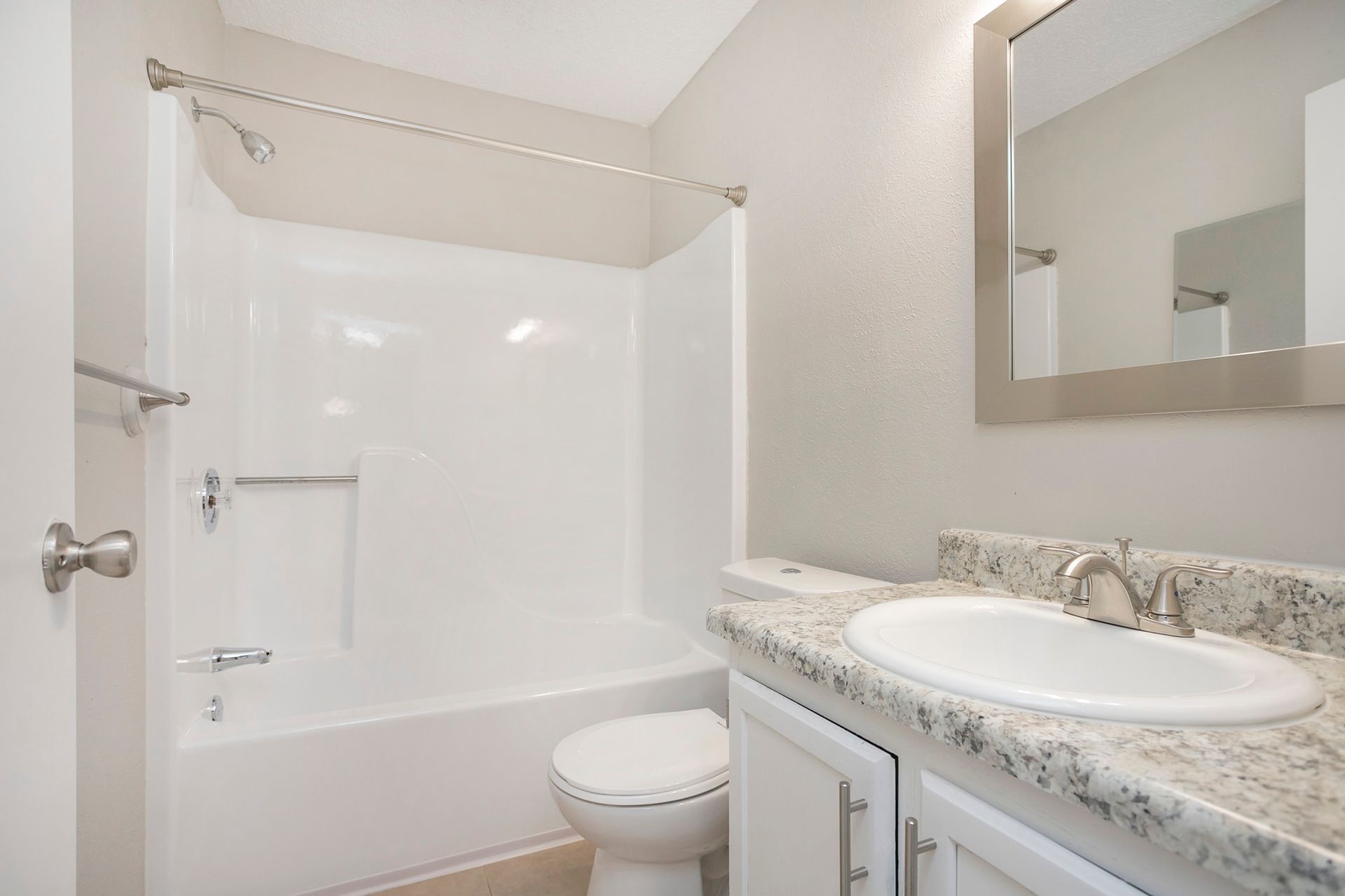 A clean, modern bathroom with a white bathtub-shower combo, toilet, and granite vanity with a sink and mirror.