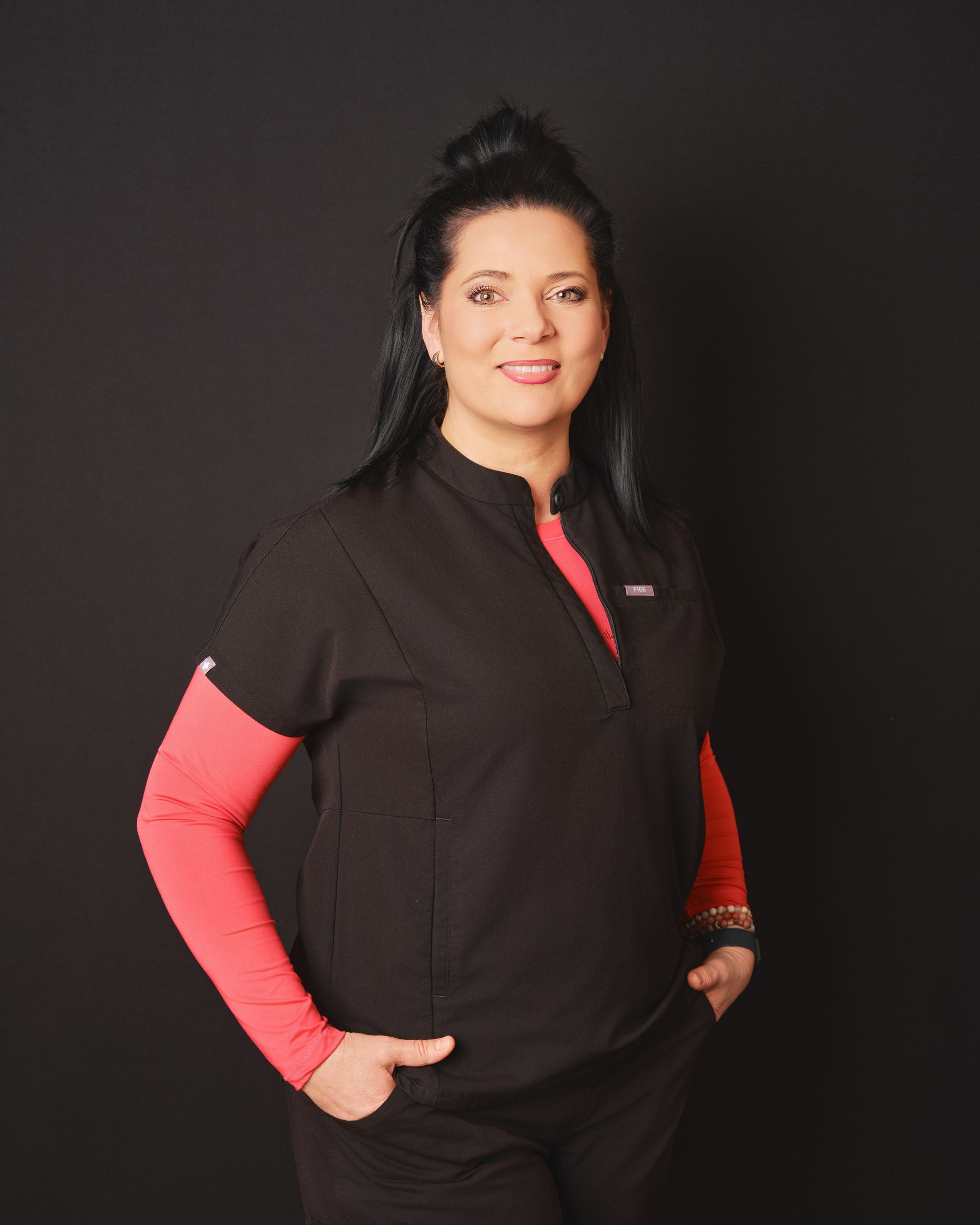 Une femme vêtue d un haut noir et de manches rouges sourit devant la caméra.