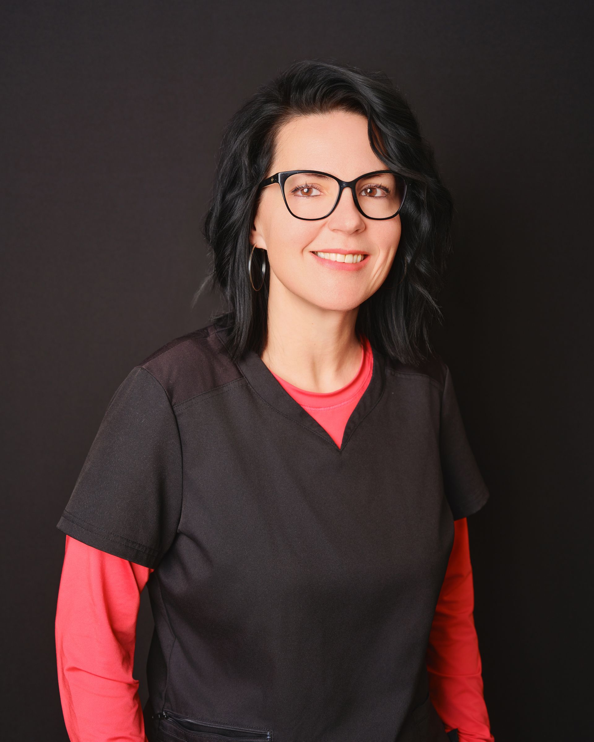 Une femme portant des lunettes et un haut noir est debout, les bras croisés.