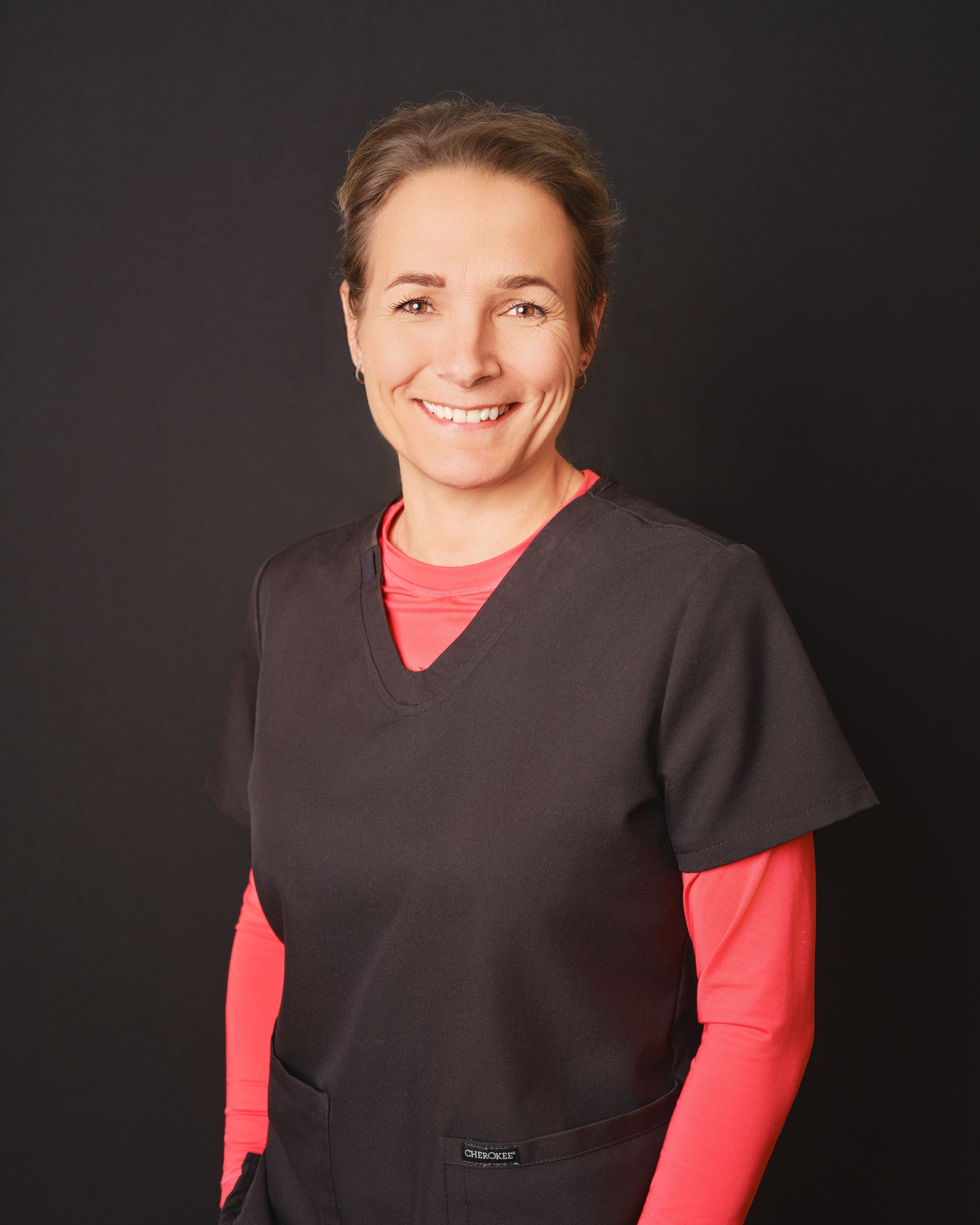 Une femme portant un haut noir et une chemise rouge sourit à la caméra.