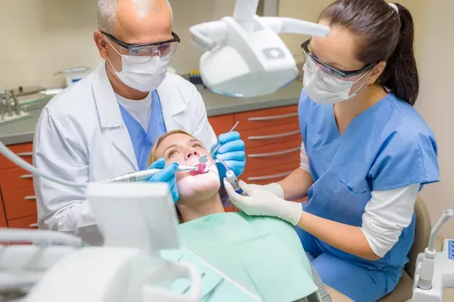 Une femme fait examiner ses dents par deux dentistes dans un cabinet dentaire.