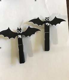 Two black bat-shaped clothespins with white eyes on a light background