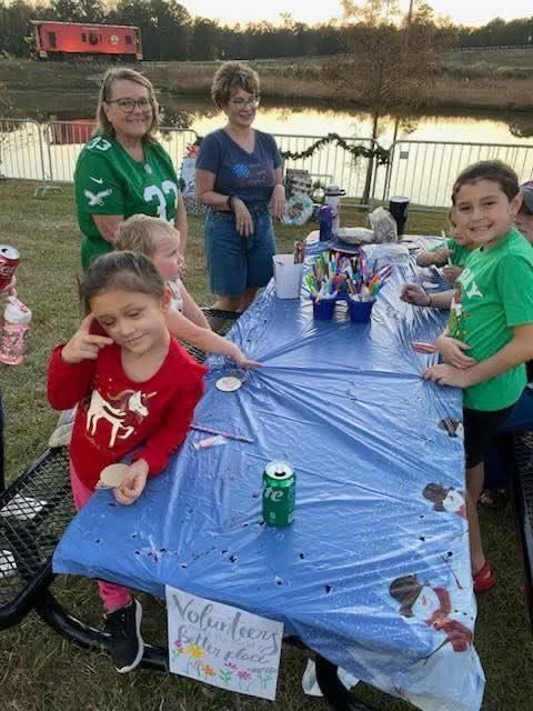 Children gathered around a blue picnic table with drinks at an outdoor backyard gathering near a pond