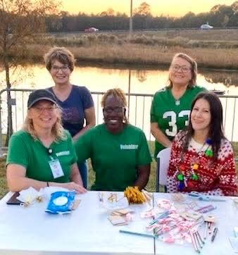 Four volunteers smile behind a table of snacks and candy by a lakeside at sunset.