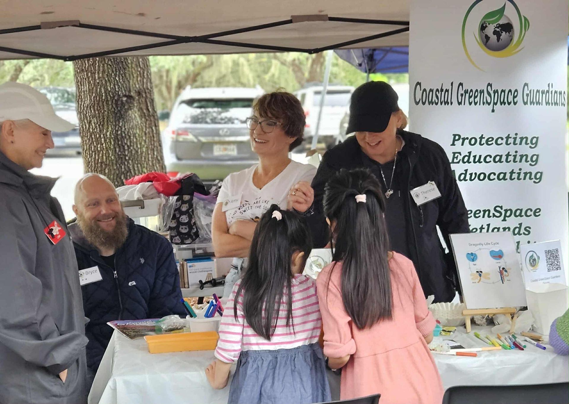 Outdoor Coast/Space support booth with volunteers speaking to children at a table under a canopy.