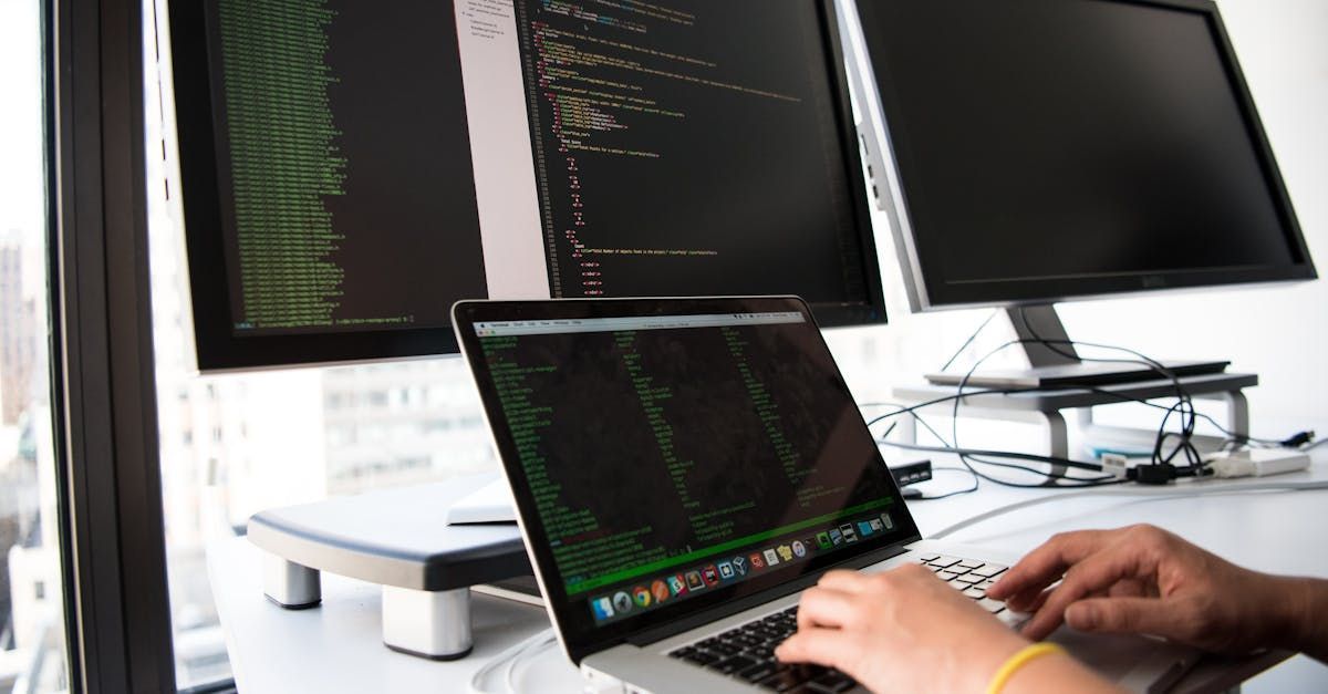 A person is typing on a laptop computer in front of three monitors.
