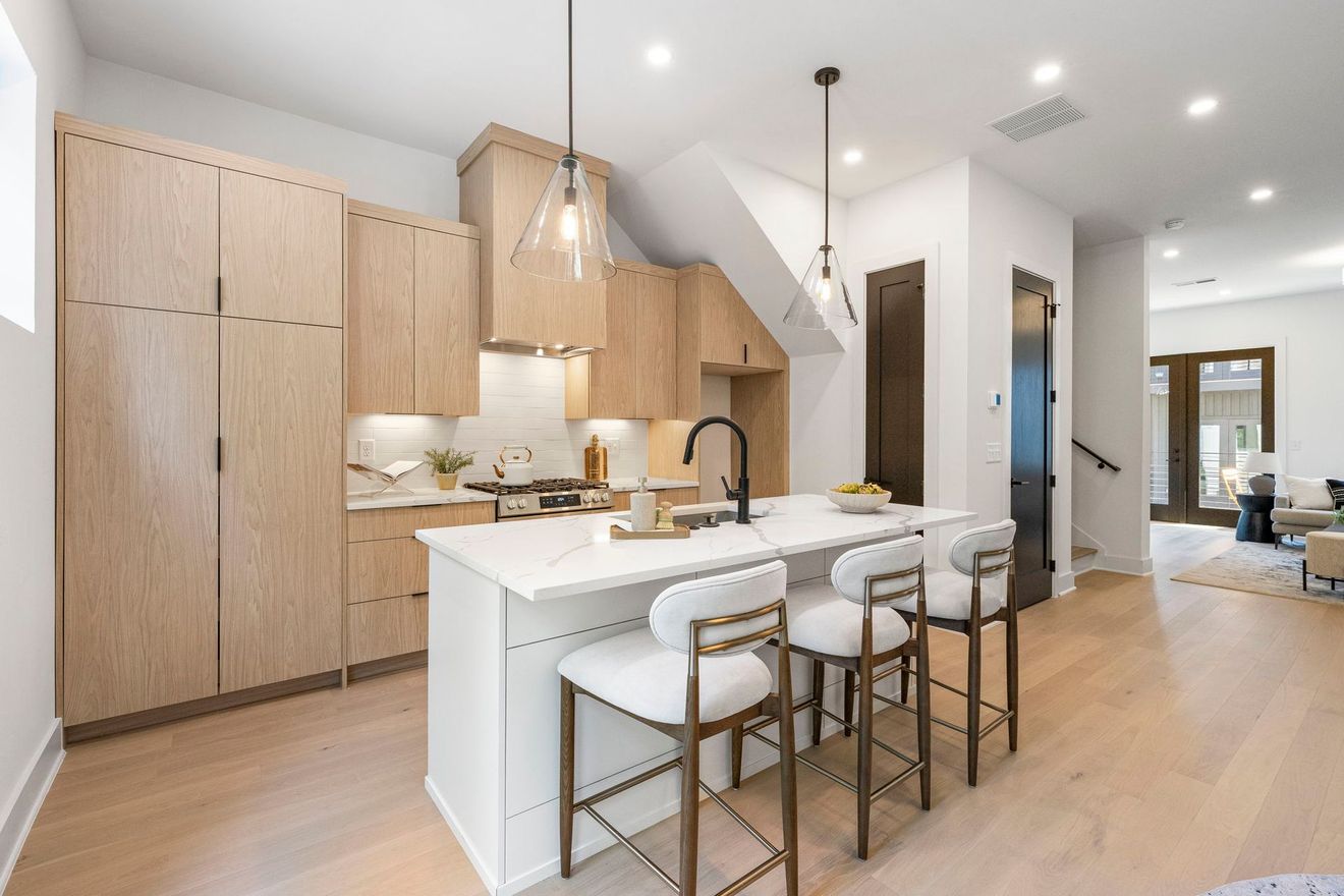 Modern kitchen with light wood cabinets, white island, pendant lights, and barstools in a bright open-plan home