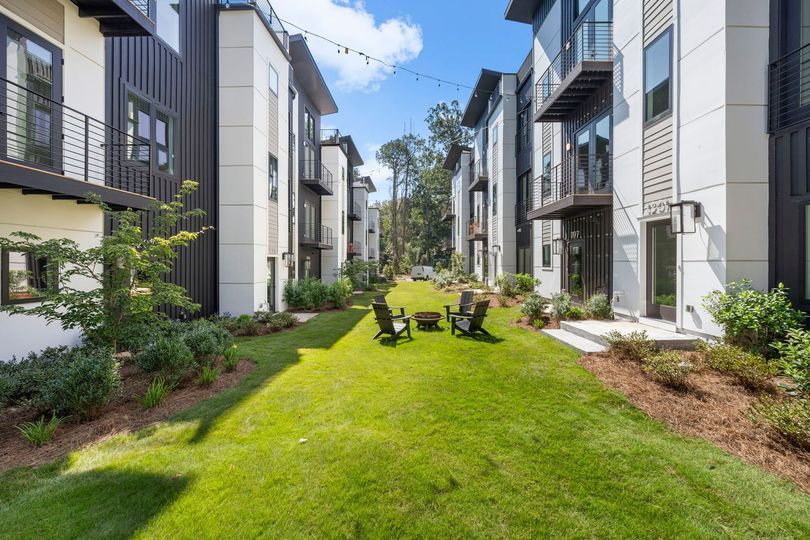 Modern apartment courtyard with green lawn, shrubs, and rows of buildings on both sides