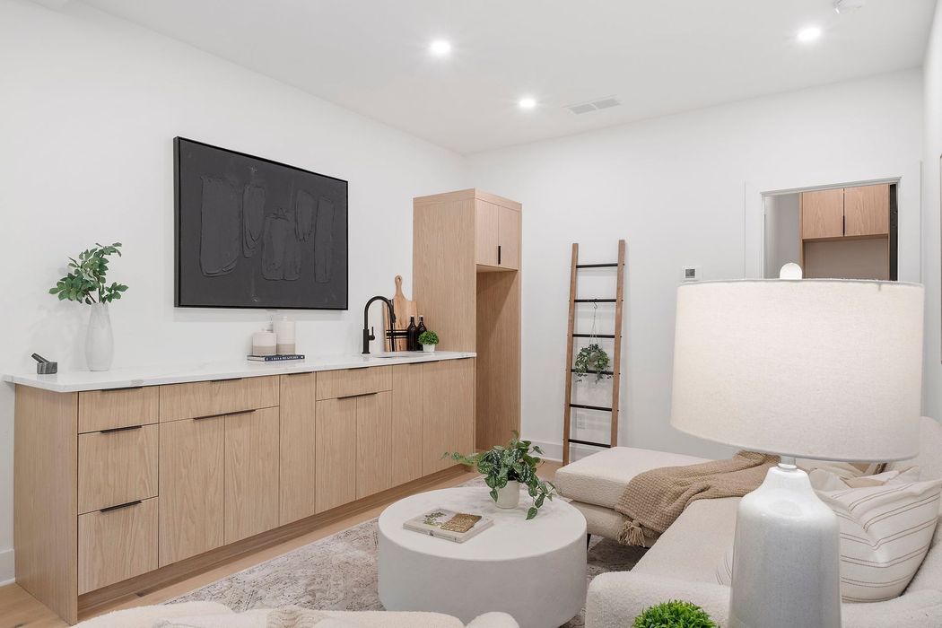 Bright minimalist living room with wood cabinets, white sofa, round table, lamp, and ladder shelf.