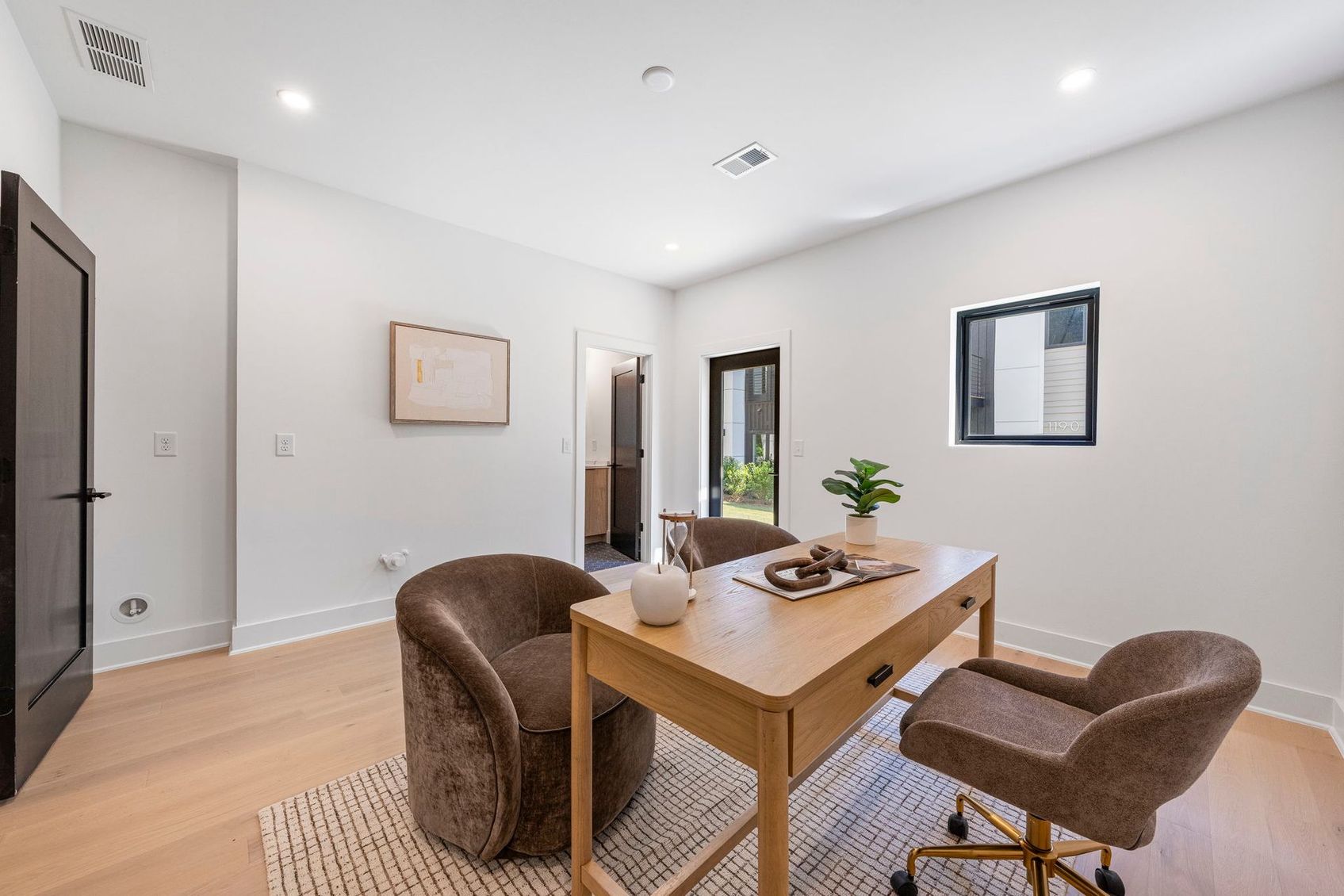 Bright modern room with desk, two chairs, wall mirror, and potted plant on the table